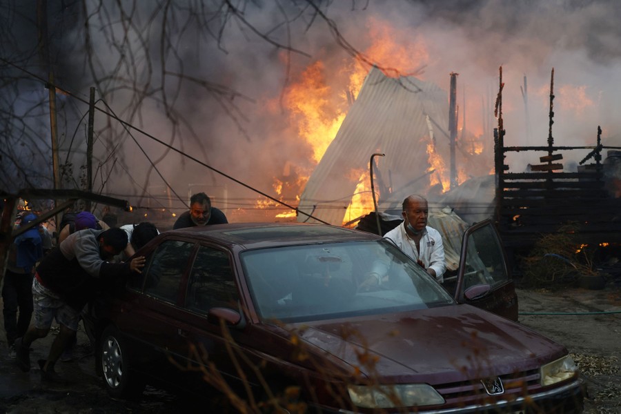 People push a car away from a burning forest fire.