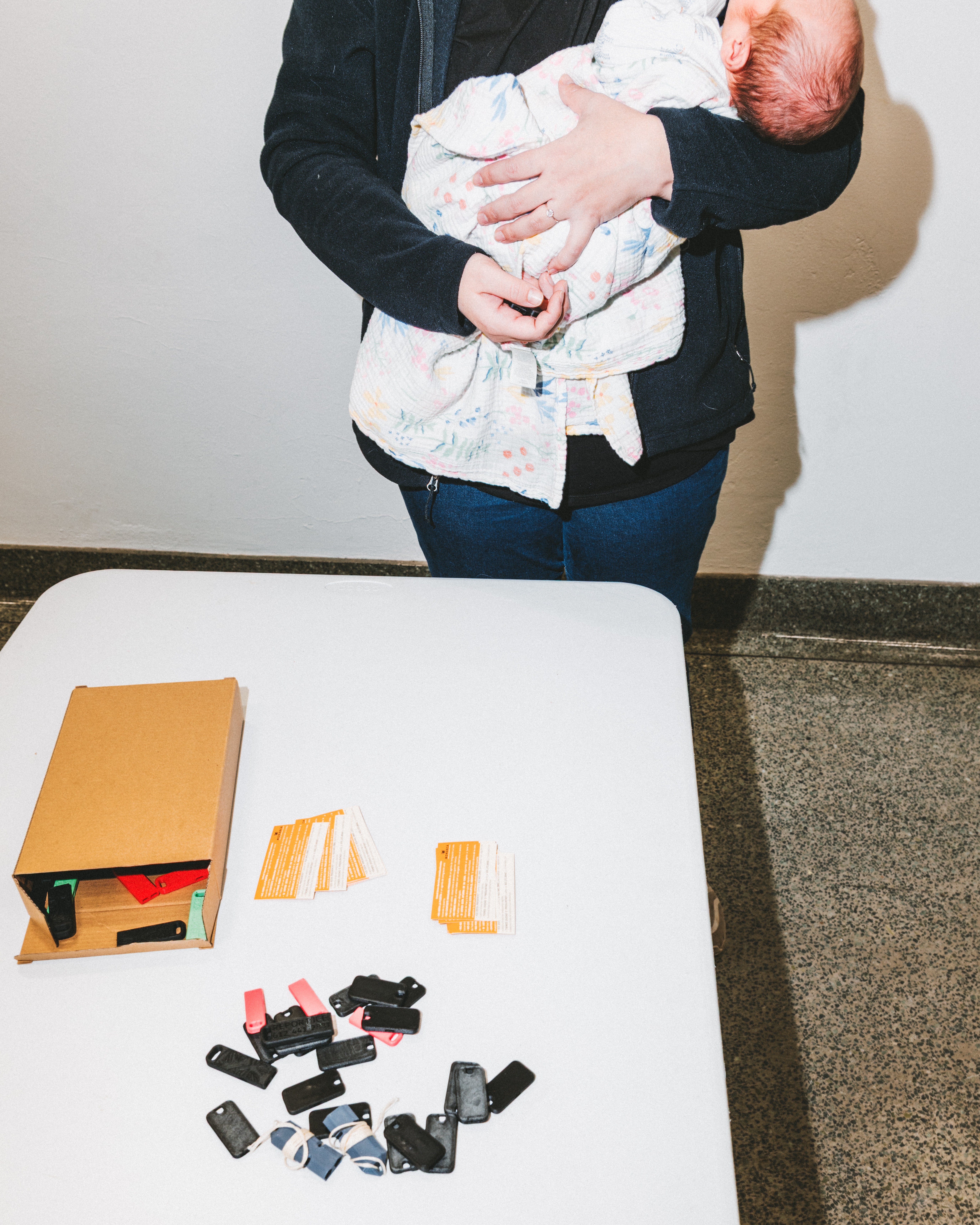 A woman holding a baby stands in front of a table with ICE whistles on it