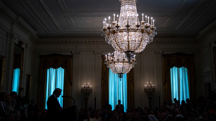 Trump speaks in a room with big chandeliers