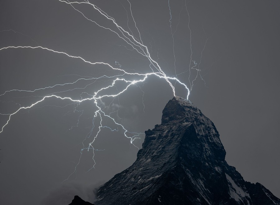 Multiple lightning strikes illuminate a stark mountaintop at night.