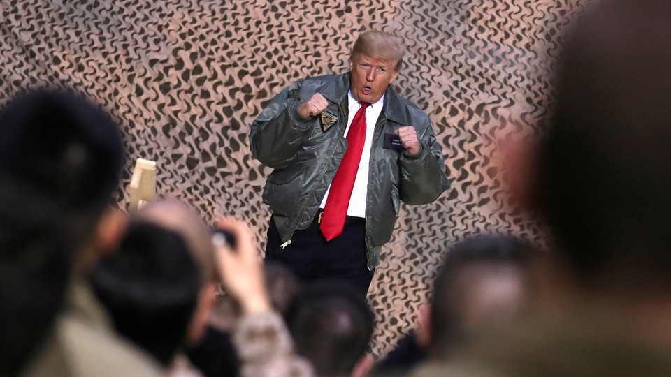 Donald Trump poses in front of cameras and U.S. troops.