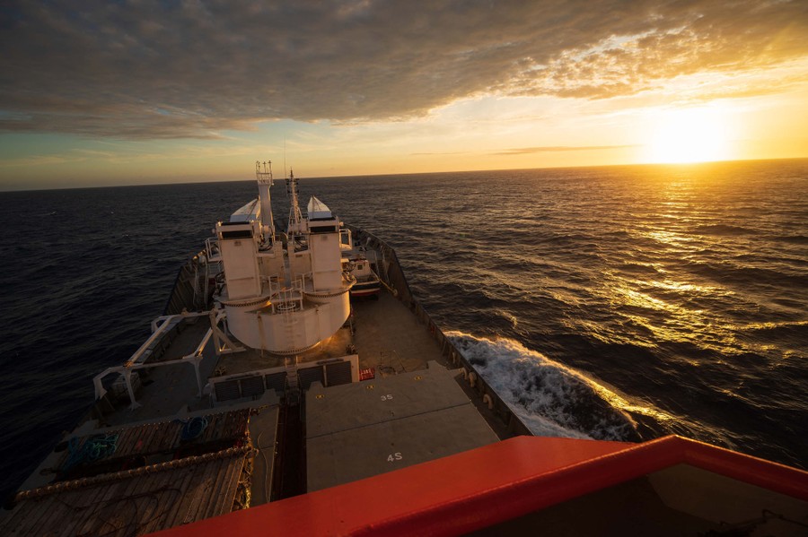 A low sun is seen over the ocean from the deck of a ship.