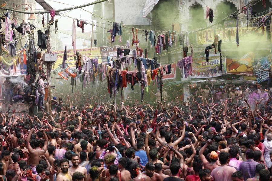 Hundreds of people celebrate in a square, dancing and throwing colored powder in the air.