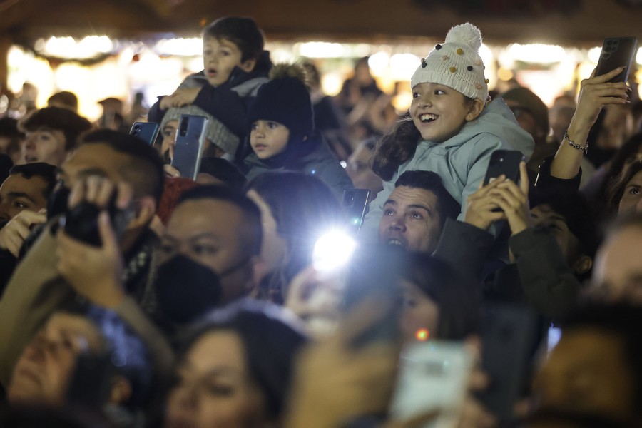 A crowd, including several children seated on the shoulders of adults, looks on in awe.