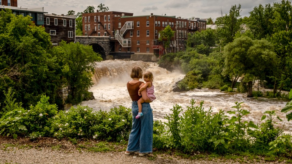 Photograph of a mother holding her daughter in front of an overflowing river in Vermont