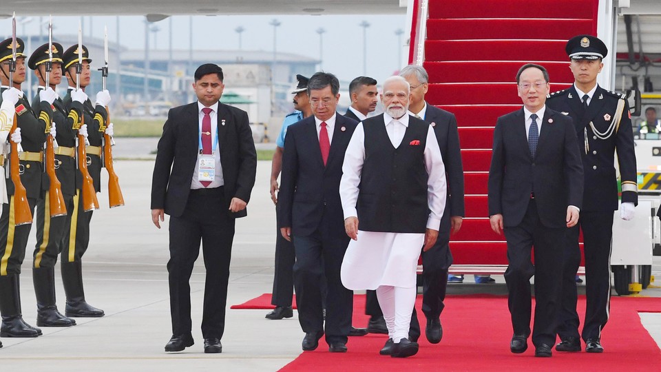 A color photo of Indian Prime Minister Narendra Modi walking on a red carpet after deplaning at a summit in China.