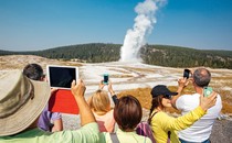 photo of crowd of people holding up phones and tablets to take pictures of geyser spout