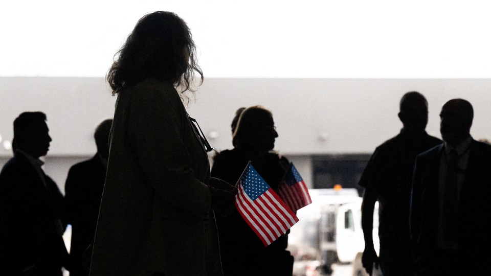 A group of people are silhouetted while holding small American flags.