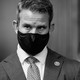 Representative Adam Kinzinger wears a black mask and suit
