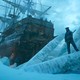A color film still from "Frankenstein," showing a man standing guard on an iceberg next to a large boat under cloudy skies.