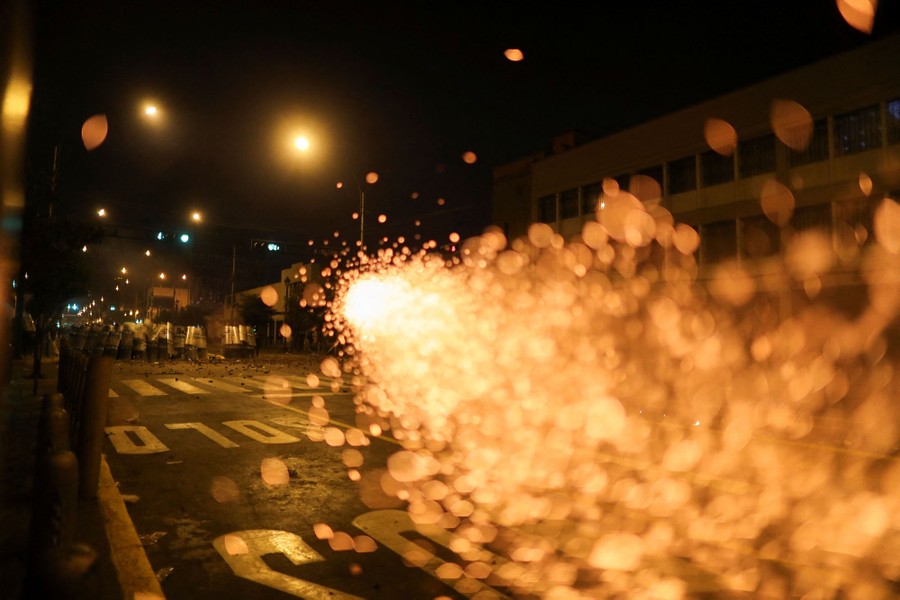 Sparks fill the scene, with riot police on a city street in the background.