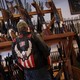 A man in a jacket featuring a bald eagle and the American flag stands in front a collection of rifles.