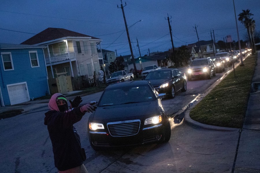 A person directs a long line of cars in a residential street.