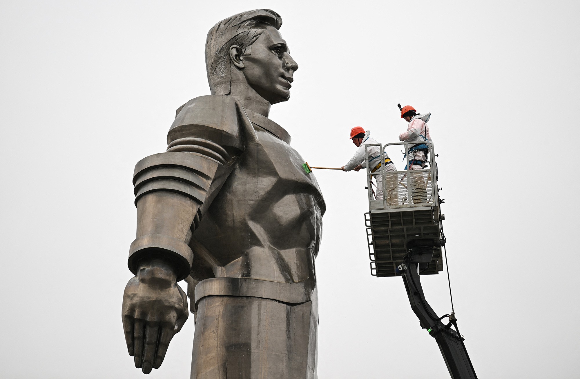 Two maintenance workers clean a tall monument of Soviet cosmonaut Yuri Gagarin.