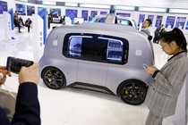 People stand indoors near a silver self-driving car.