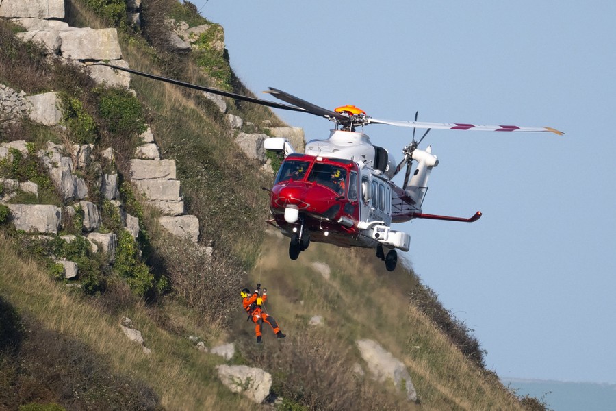A coast-guard rescue helicopter raises a winch paramedic during a training exercise.