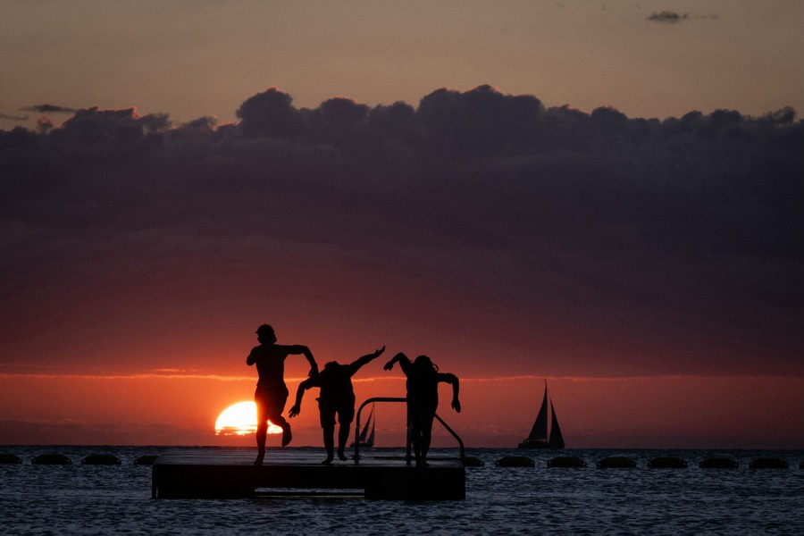 People dive from a platform in the sea at sunset.