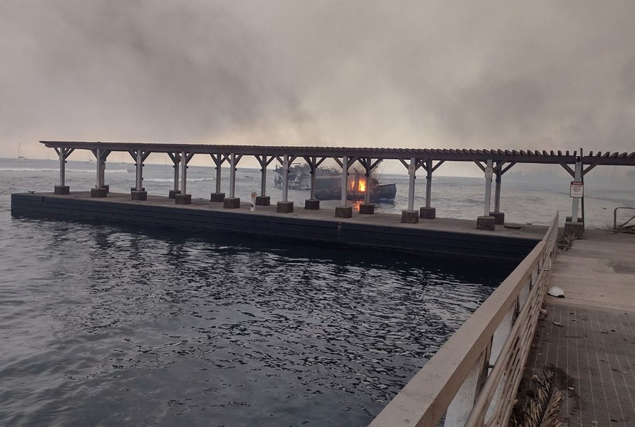 A small boat burns, floating near a pier.