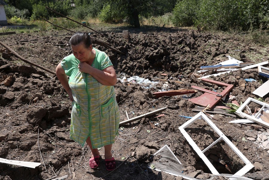 A woman stands next to a crater caused by Russian bombardment outside her house.