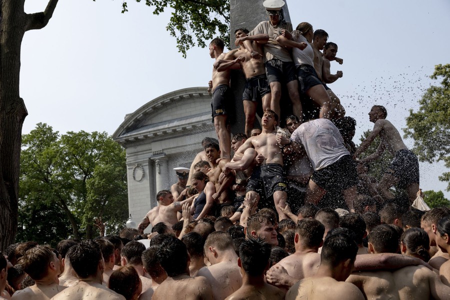 A crowd of young people pushes together and lifts one another high up an obelisk.
