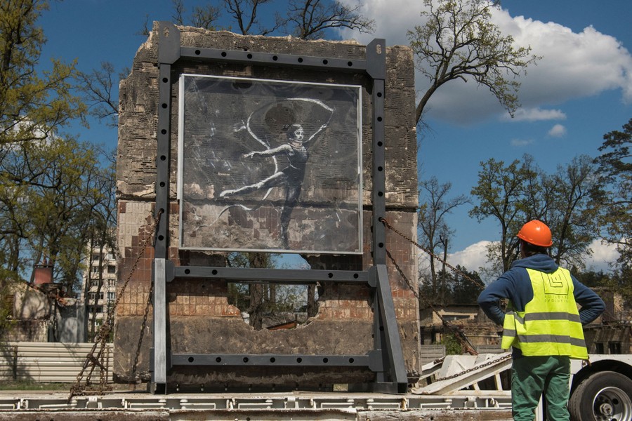 A worker looks at a part of a wall with a mural of a dancer, as it is moved onto a truck.