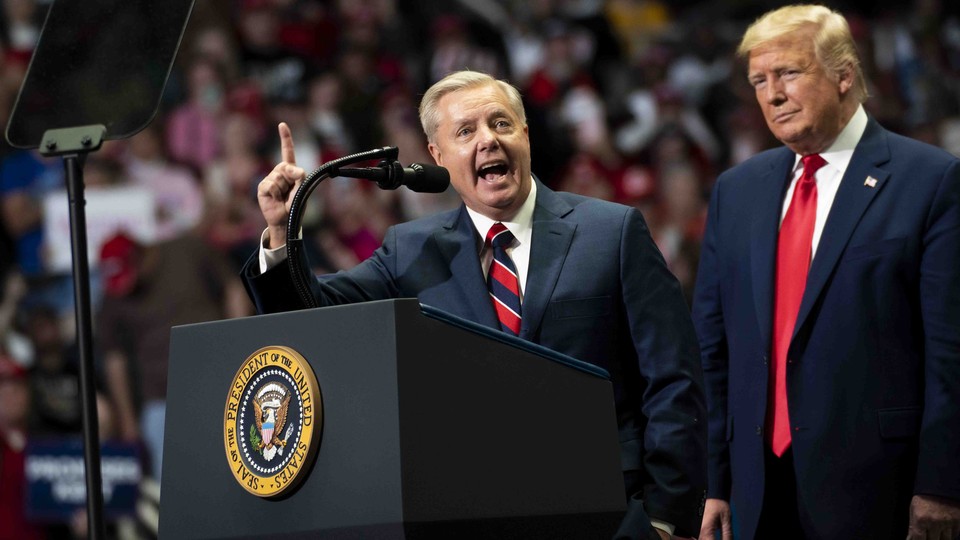 Lindsey Graham speaking at a podium with Donald Trump standing behind him. Podium has a POTUS seal on it.