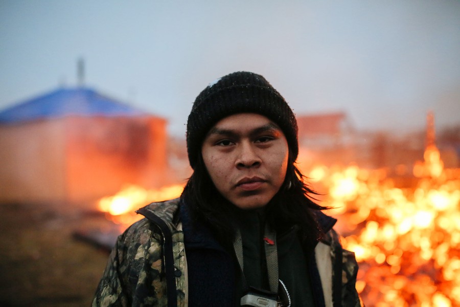 O'Shea Spencer, 20, stands in front of the remains of a hogan structure. Campers set structures on fire in preparation for the Army Corp's 2 p.m. deadline to leave the Oceti Sakowin protest camp on February 22, 2017 in Cannon Ball, North Dakota. Activists and protesters have occupied the Standing Rock Sioux reservation for months in opposition to the completion of the Dakota Access Pipeline.