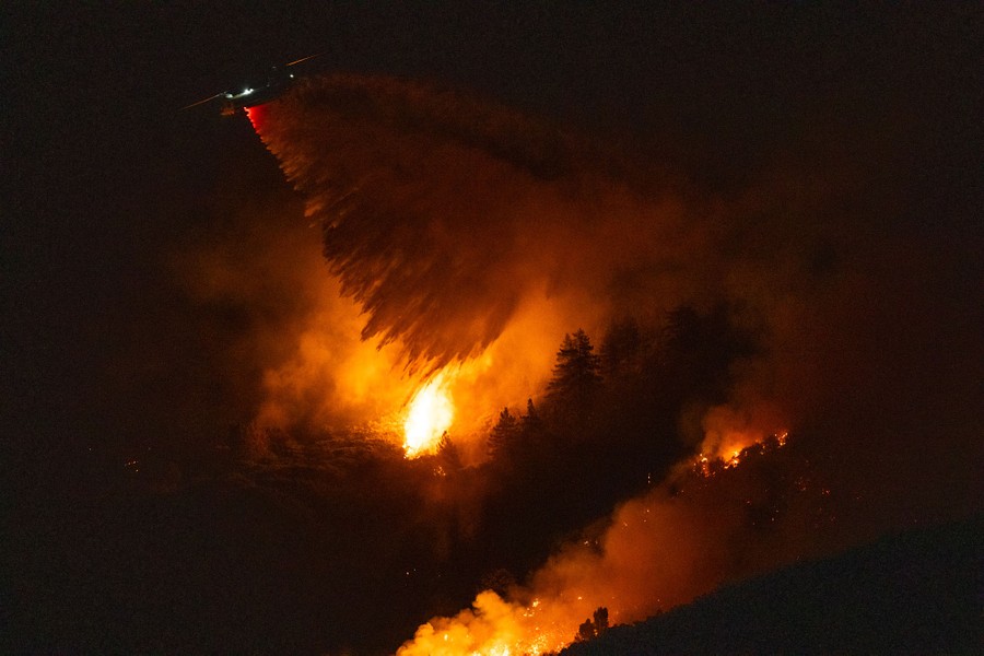 A firefighting helicopter drops a plume of water onto a burning forest at night.