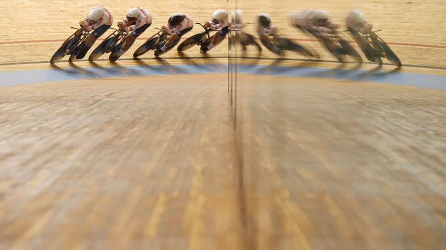 Four racing cyclists round a track, lined up one in front of the other.