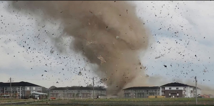 A vortex of wind throws dust and debris into the air above apartment buildings.