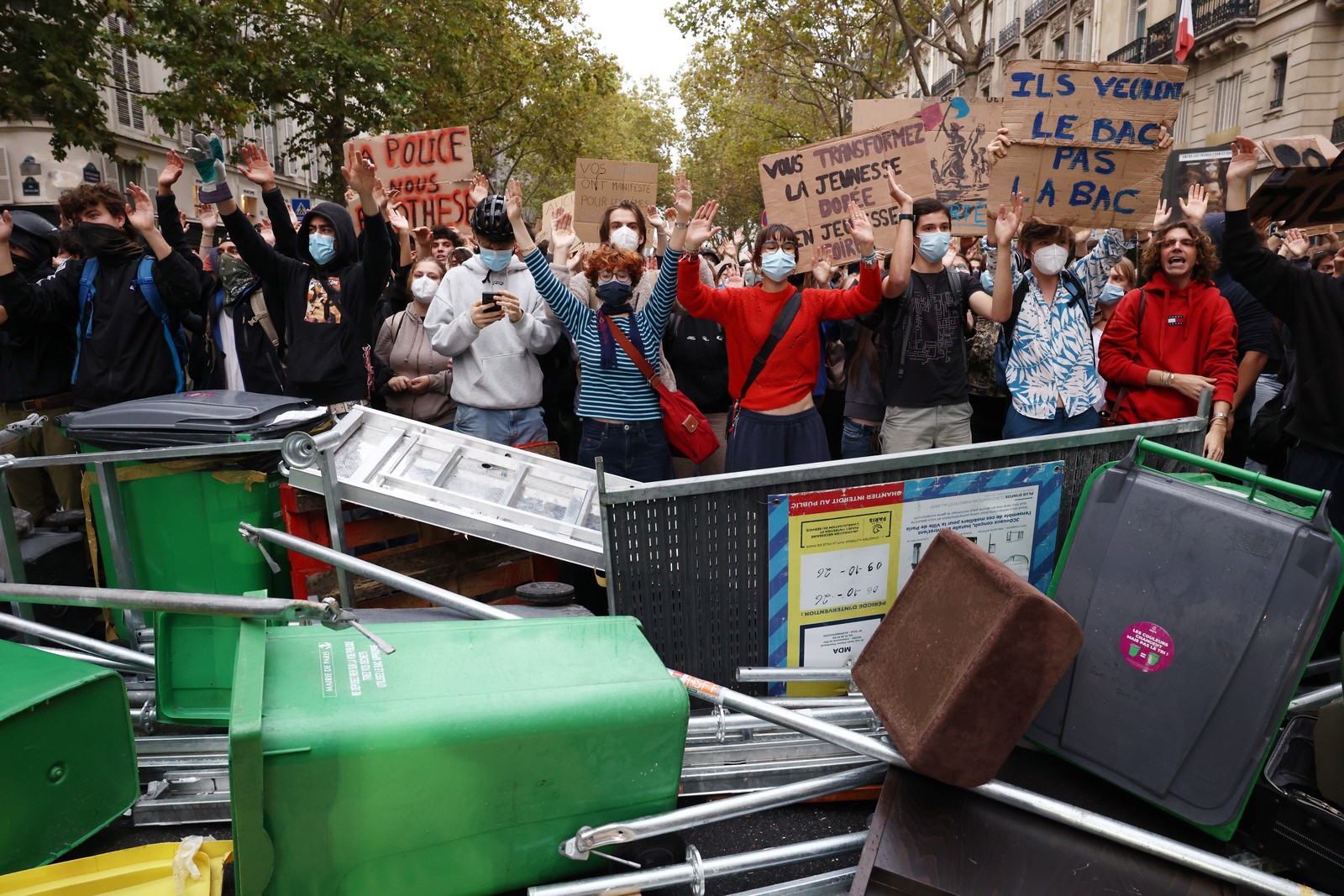 Student protesters stand together in a street behind a makeshift barricade of garbage bins and scaffolding.