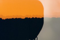 silhouette of half a man's face with two earrings against an orange horizon