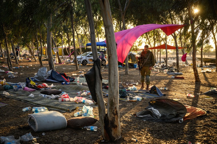 A soldier walks through a stand of trees, surrounded by abandoned blankets and camping gear.