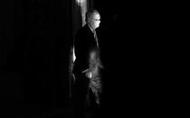 A black-and-white photo of Mitch McConnell wearing a face mask, surrounded by darkness
