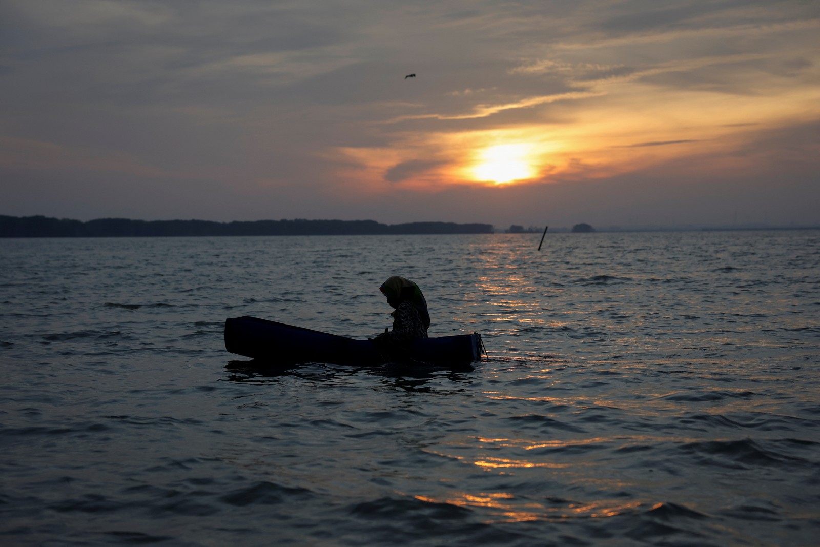 A woman floats in a small makeshift boat at sunset.