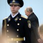 A member of the Russian military stands at attention. Behind him, Putin walks past.