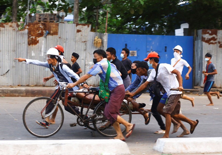 Several people run alongside a tricycle, carrying an injured person.