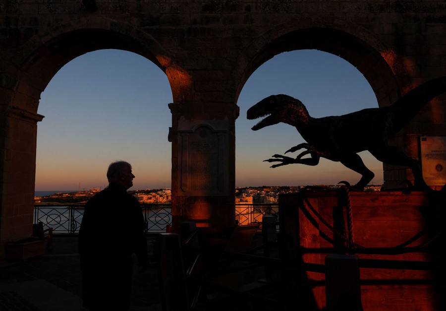 A person looks at a large model of a dinosaur near an archway.