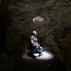 A man looks up through a hole at the top of a cave.