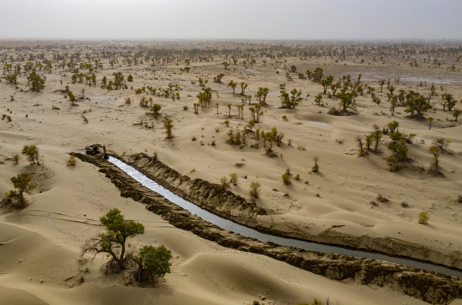 An excavator works at one end of a newly-dug canal through a desert area.