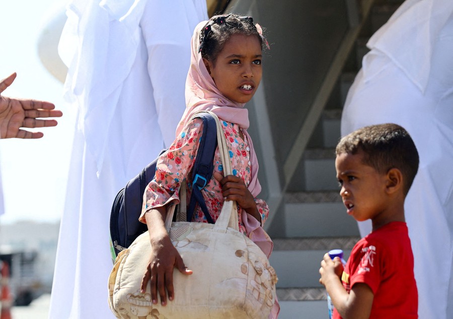 Two children stand near steps on an airport runway.