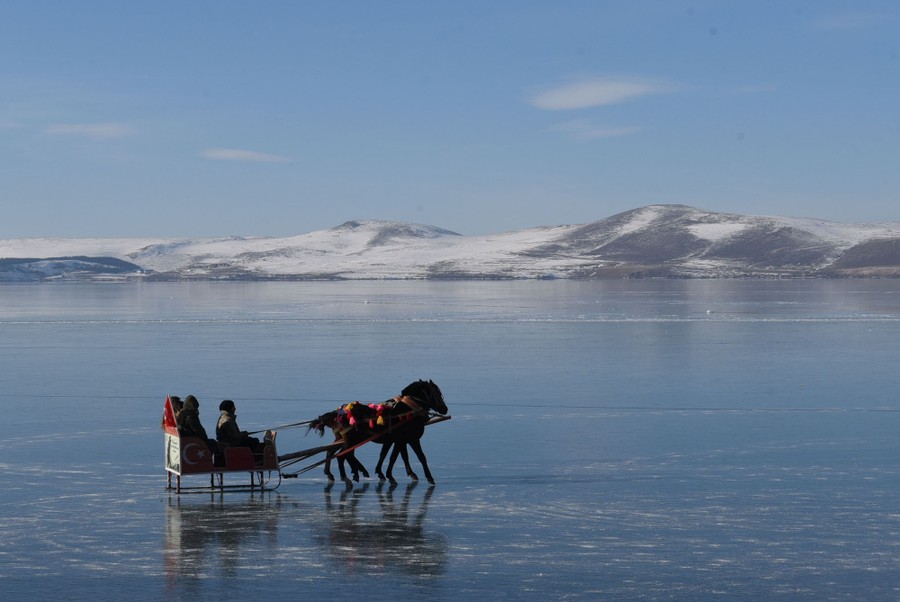 Several people ride in a small sleigh pulled by two horses across a frozen lake.