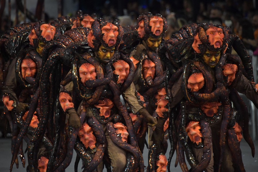 Several dancers wear costumes with multiple faces and tentacles.