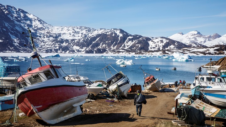 A man walks among boats with snow-covered mountains in the distance.