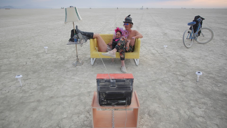 Two people sitting on a yellow sofa watching TV at Burning Man