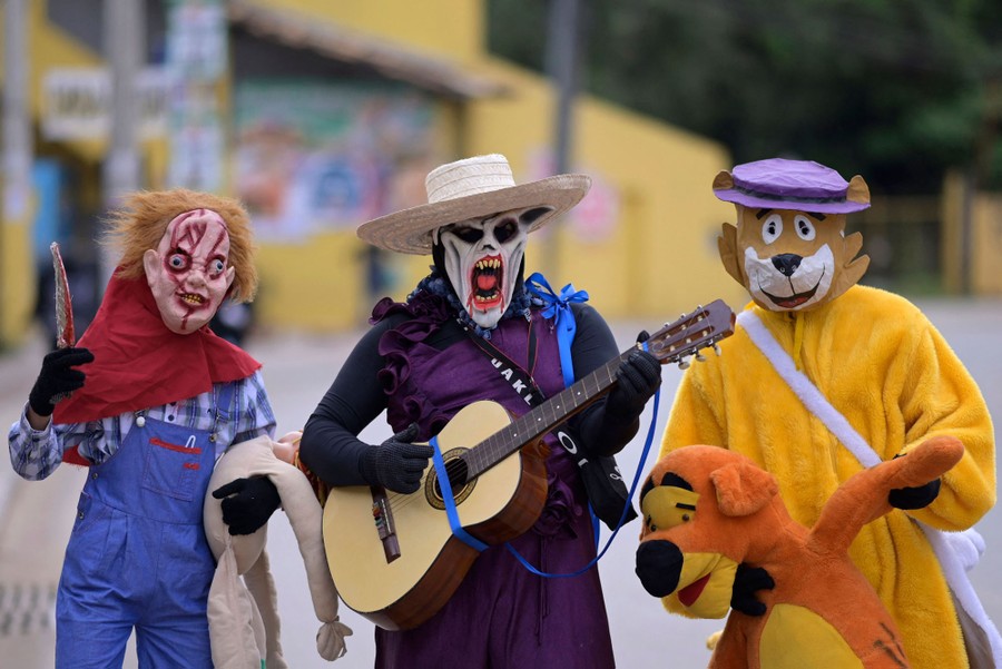 Three people in colorful and odd costumes stand together in a street.
