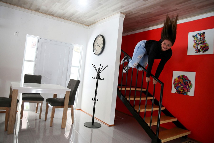 A woman hangs from the railing of a staircase inside a house that was built upside down as an attraction—the photo has been rotated to make the woman appear to be defying gravity.