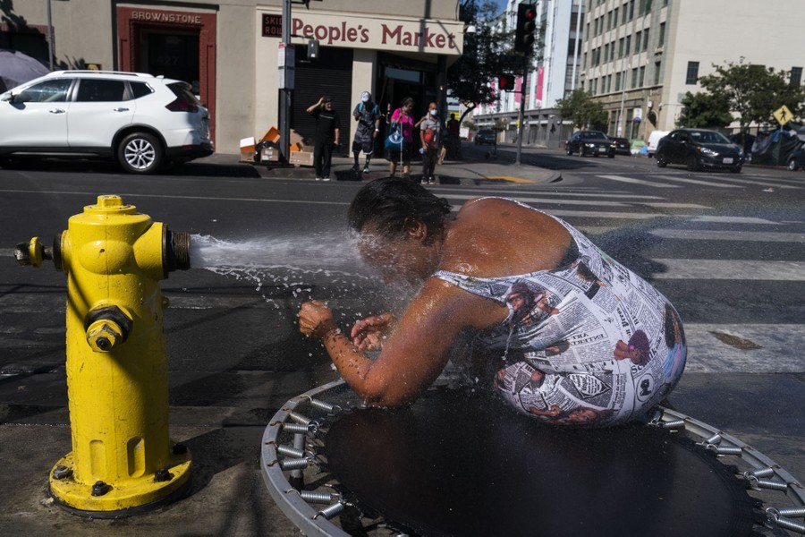 A woman leans low, sticking her head into a stream of water from a fire hydrant.