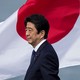 Former Japanese Prime Minister Shinzo Abe, wearing a navy suit and standing in front of the Japanese flag