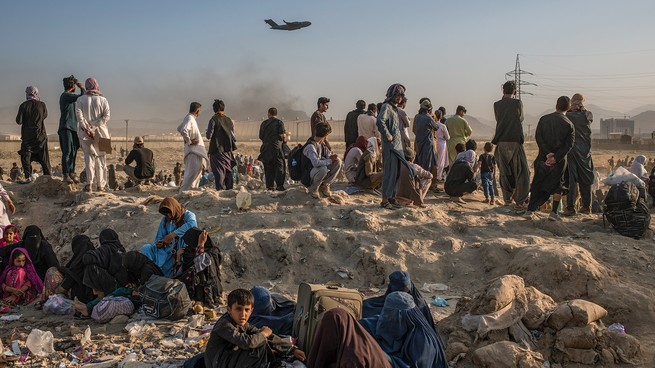 Afghans camp near Hamid Karzai International Airport, in Kabul, on August 24, a week before Joe Biden’s declared deadline for the evacuation of allies. A U.S.-military C-17 transport aircraft takes off overhead. (Andrew Quilty / Agence VU’)